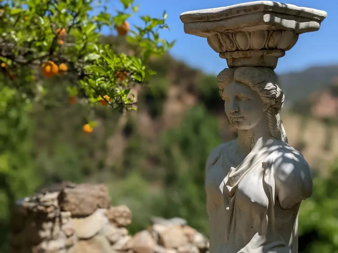 Sculpture of a woman in the botanical gardens of Crete with a vibrant orange tree in the backdrop.