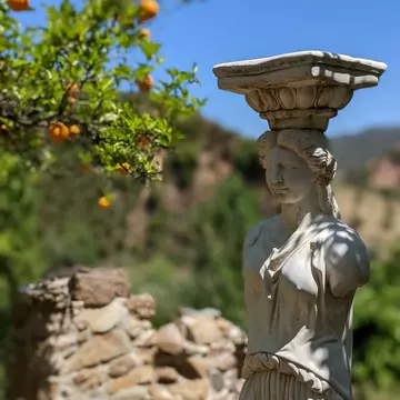Sculpture of a woman in the botanical gardens of Crete with a vibrant orange tree in the backdrop.