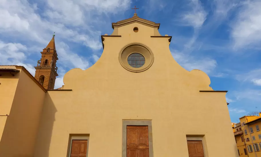 Plain cream facade of Santo Spirito basilica in Oltrarno, Florence, with round oculus, scroll gables and brick bell tower