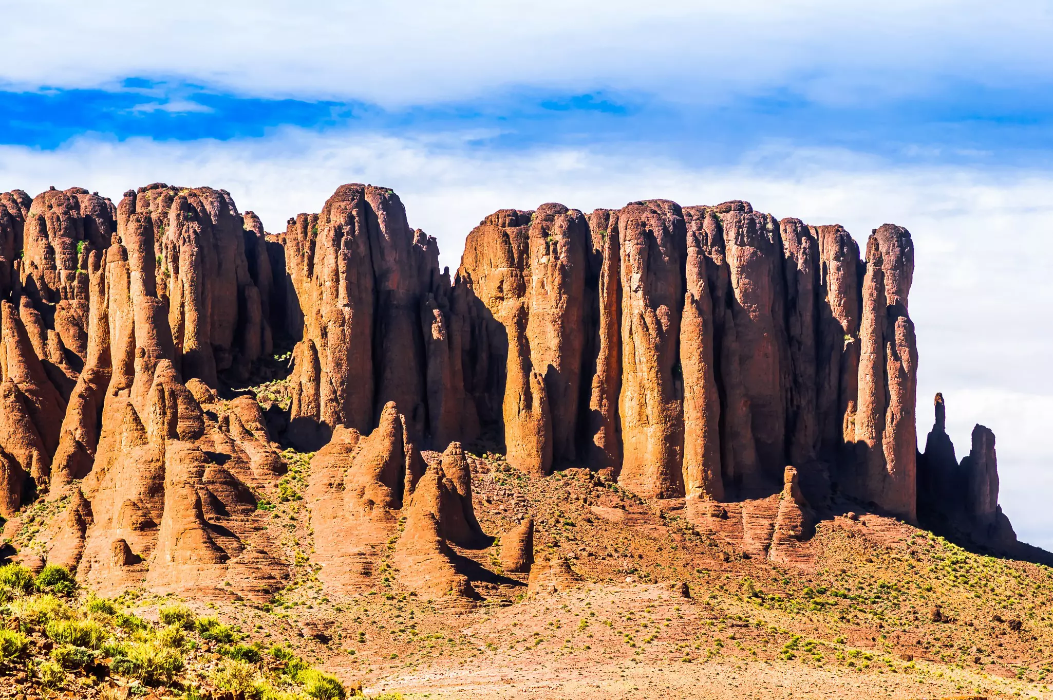 Bulbous, almost finger-like red-rock formations rise from the valley floor; the valley is dotted with green shrub-like vegetation.