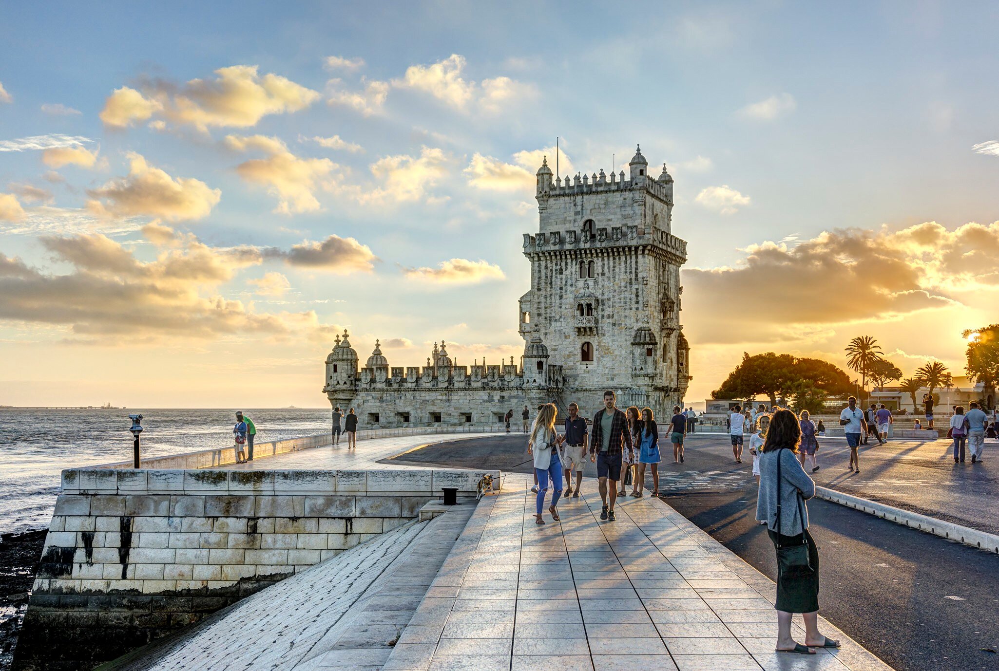 People wandering around a waterfront with a distinctive crenellated tower 