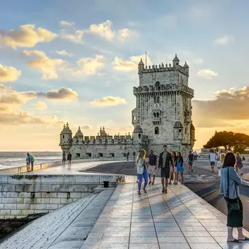 People wandering around a waterfront with a distinctive crenellated tower 