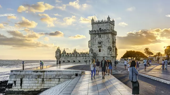 People wandering around a waterfront with a distinctive crenellated tower 