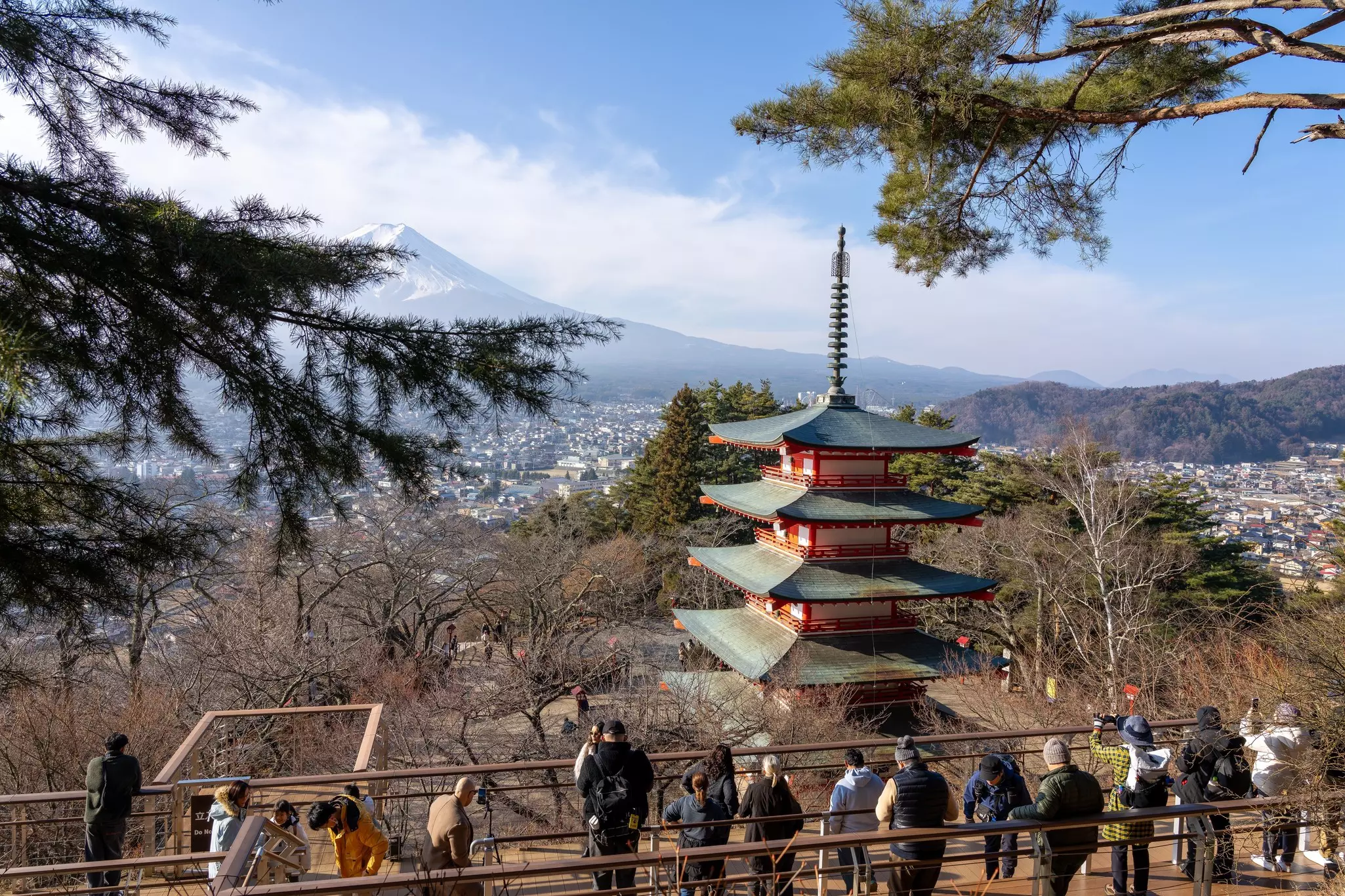 People gather at a viewpoint near a tiered temple looking towards the peak of a snowcapped mountain.