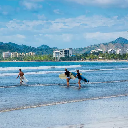 Surfers walk into the water, carrying their boards.