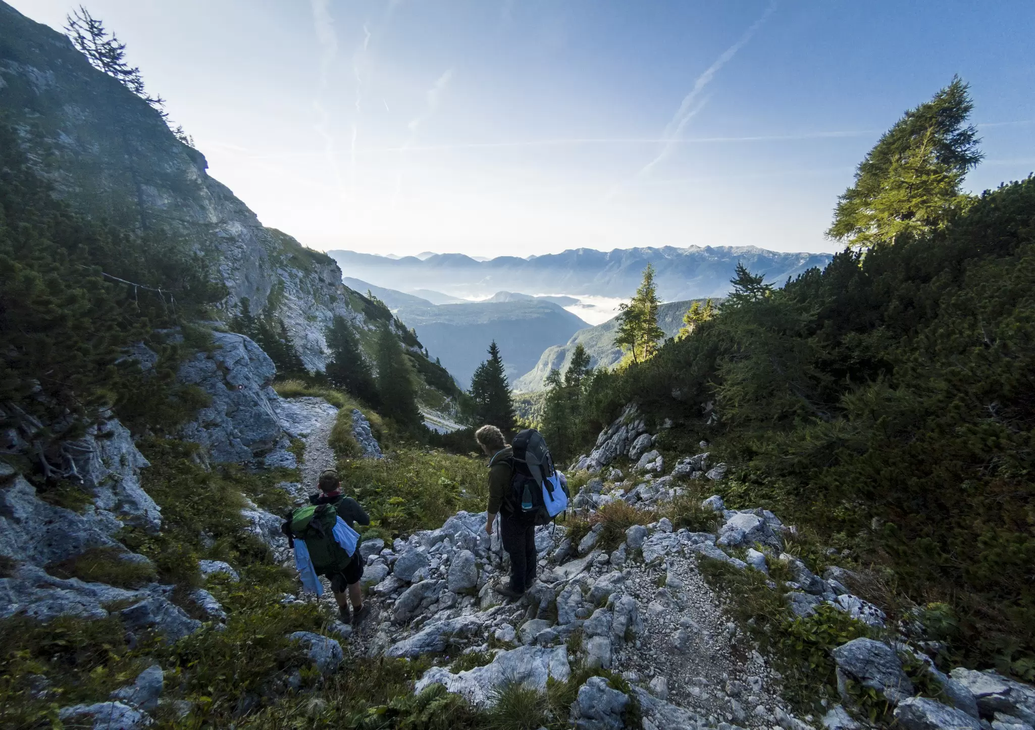 Hikers walking across uneven rocky terrain with views of mountaintops and cloud in the background.