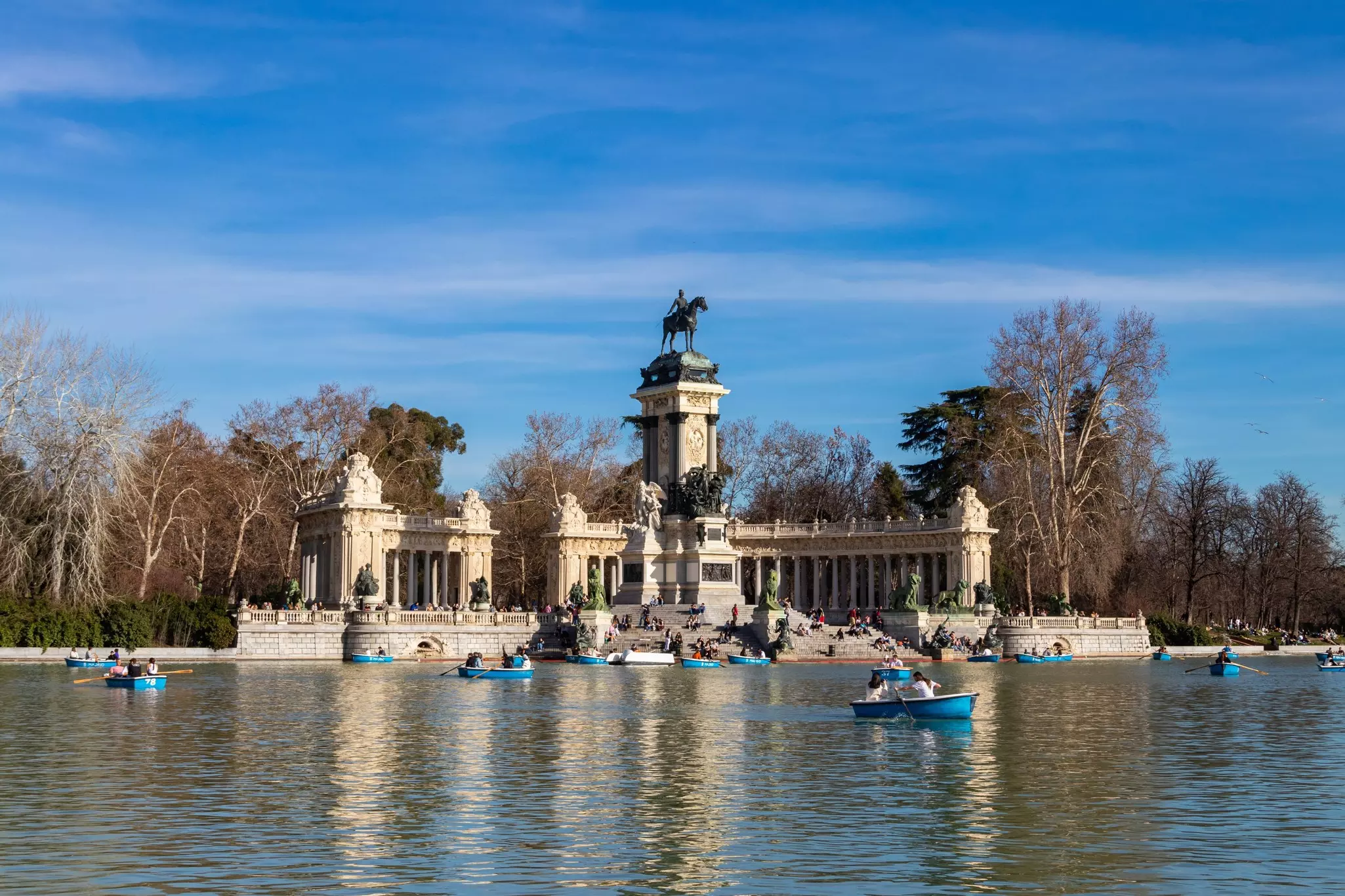 People riding small boats on great pond across from monument to King Alfonso XII at the Retiro park in Madrid, Spain.