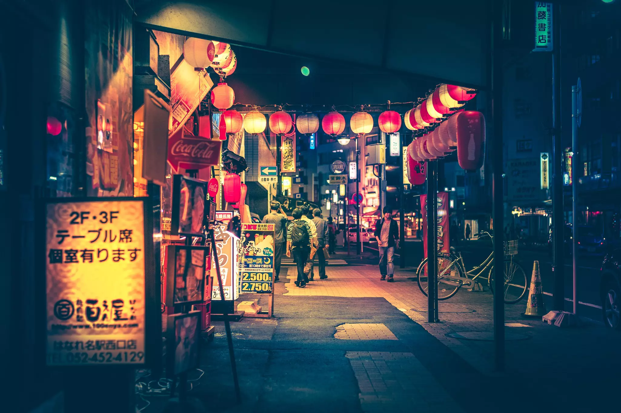 A street at night lined with bars and restaurants and decorated with glowing red paper lanterns.