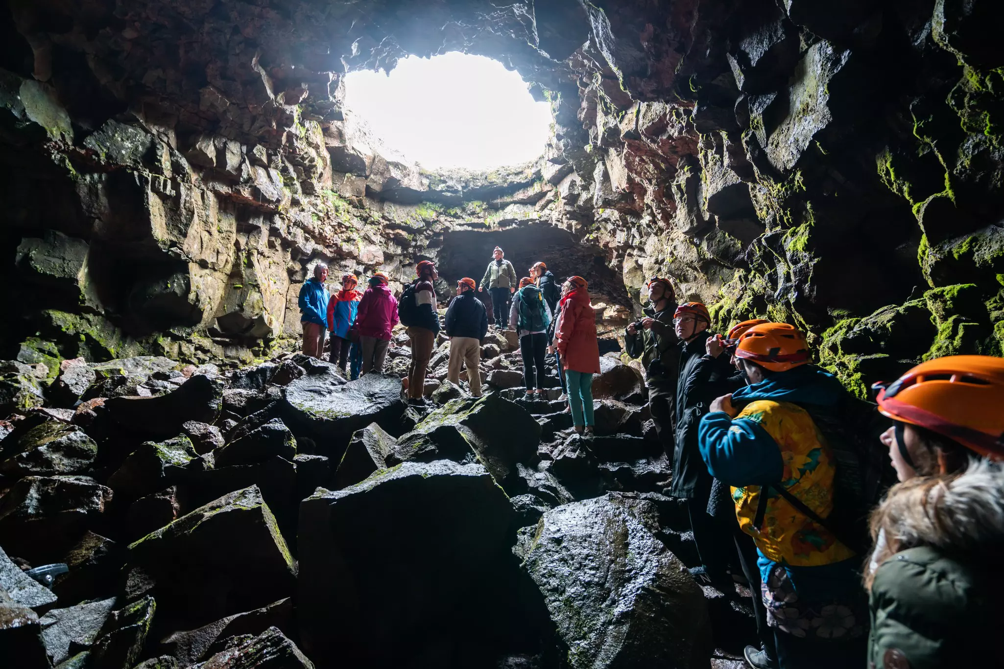 A group of people wearing caving gear in a lava tunnel cave