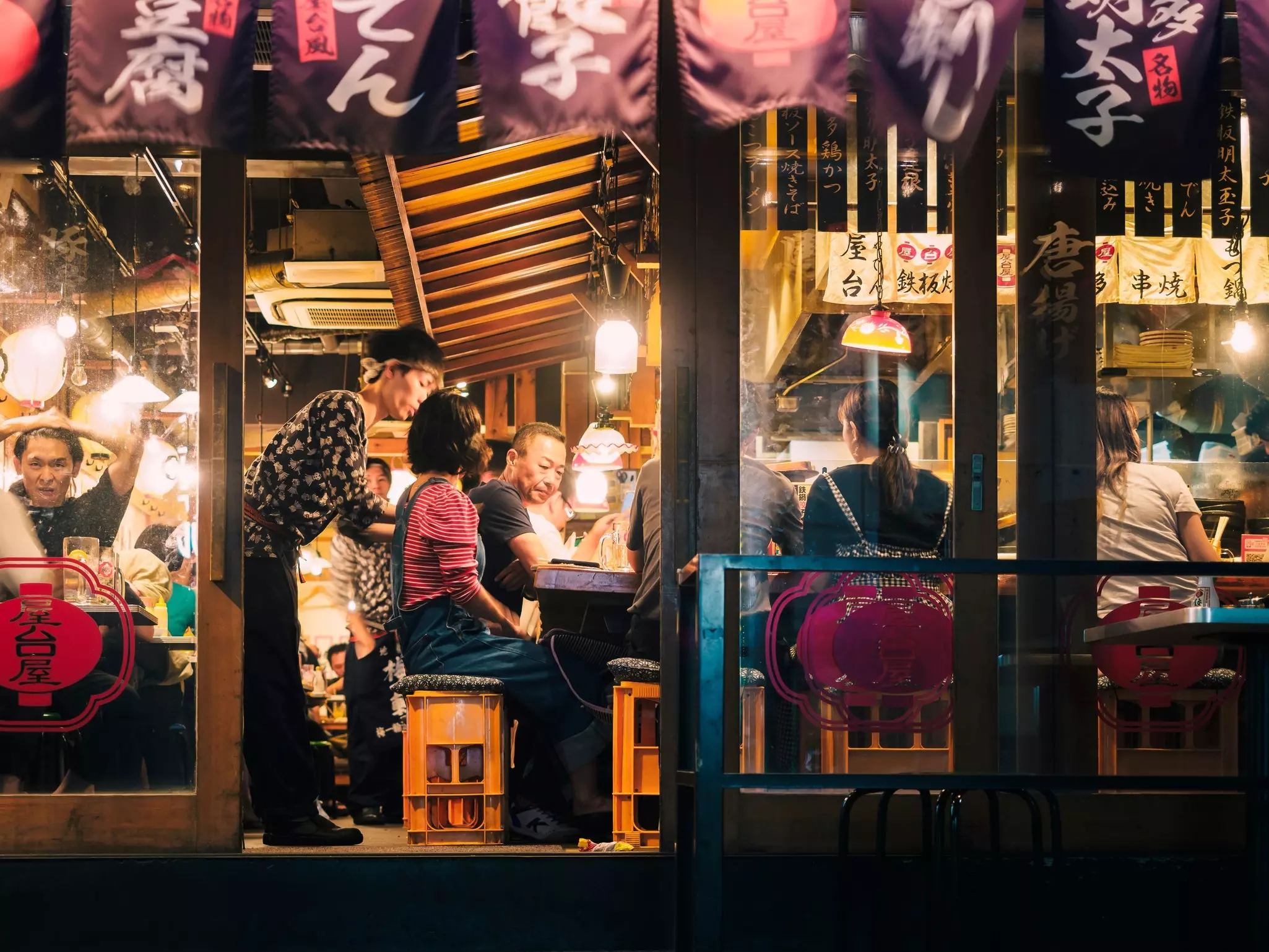 A Japanese bar filled with people at seats, drinking beer and ordering food
