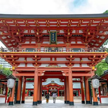 Red two-storey gate of Ikuta Shrine in Kobe with a plaque reading 生田宮, paper lanterns and the main hall seen through it